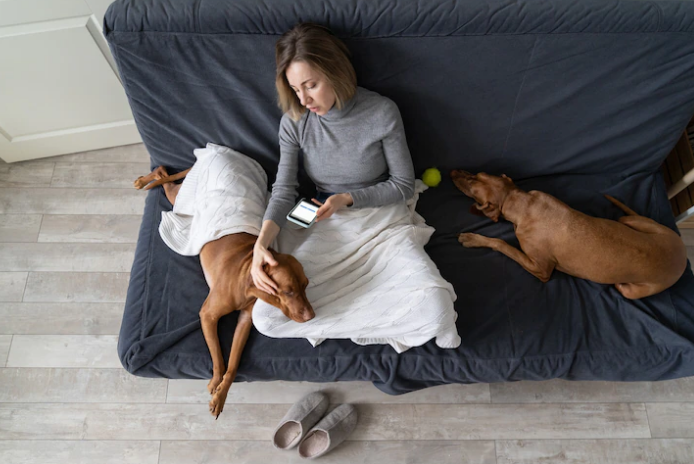 woman sitting on a couch using a smartphone while caressing her dog